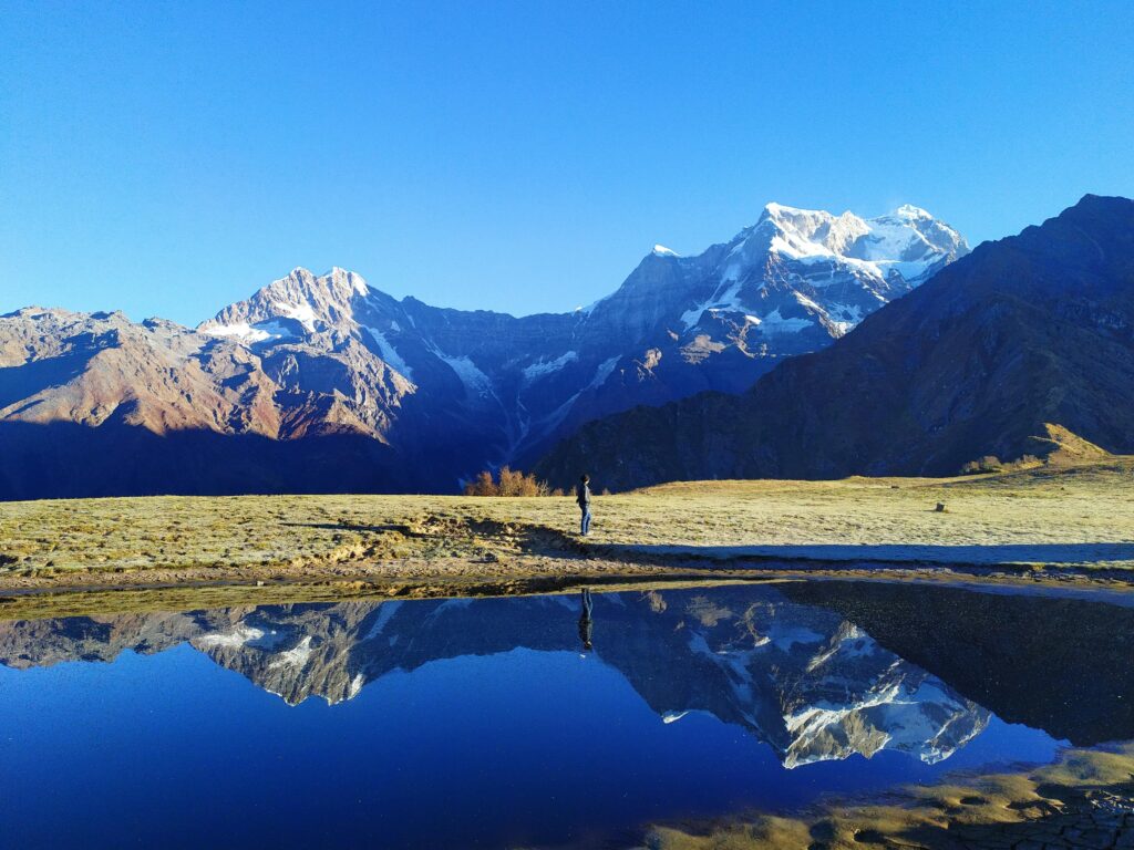 A breathtaking view of snowcapped Chaukhamba peaks reflecting in a serene pond in the Himalayas, India.